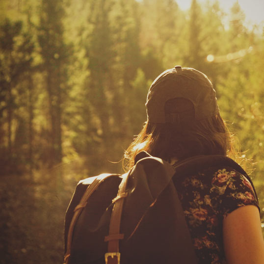 Tween with hat and backpack in tall grass with golden light